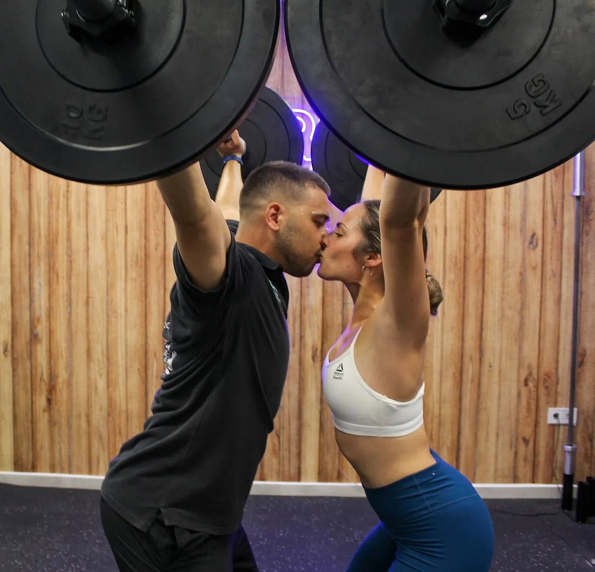 Kleos Entrenamiento pareja levanta peso dandose un piquito